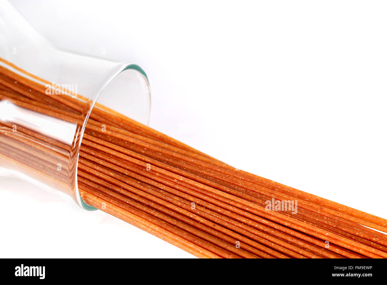 Marrone crudo intero spaghetti di grano in un barattolo di vetro giacente su sfondo bianco. Foto Stock