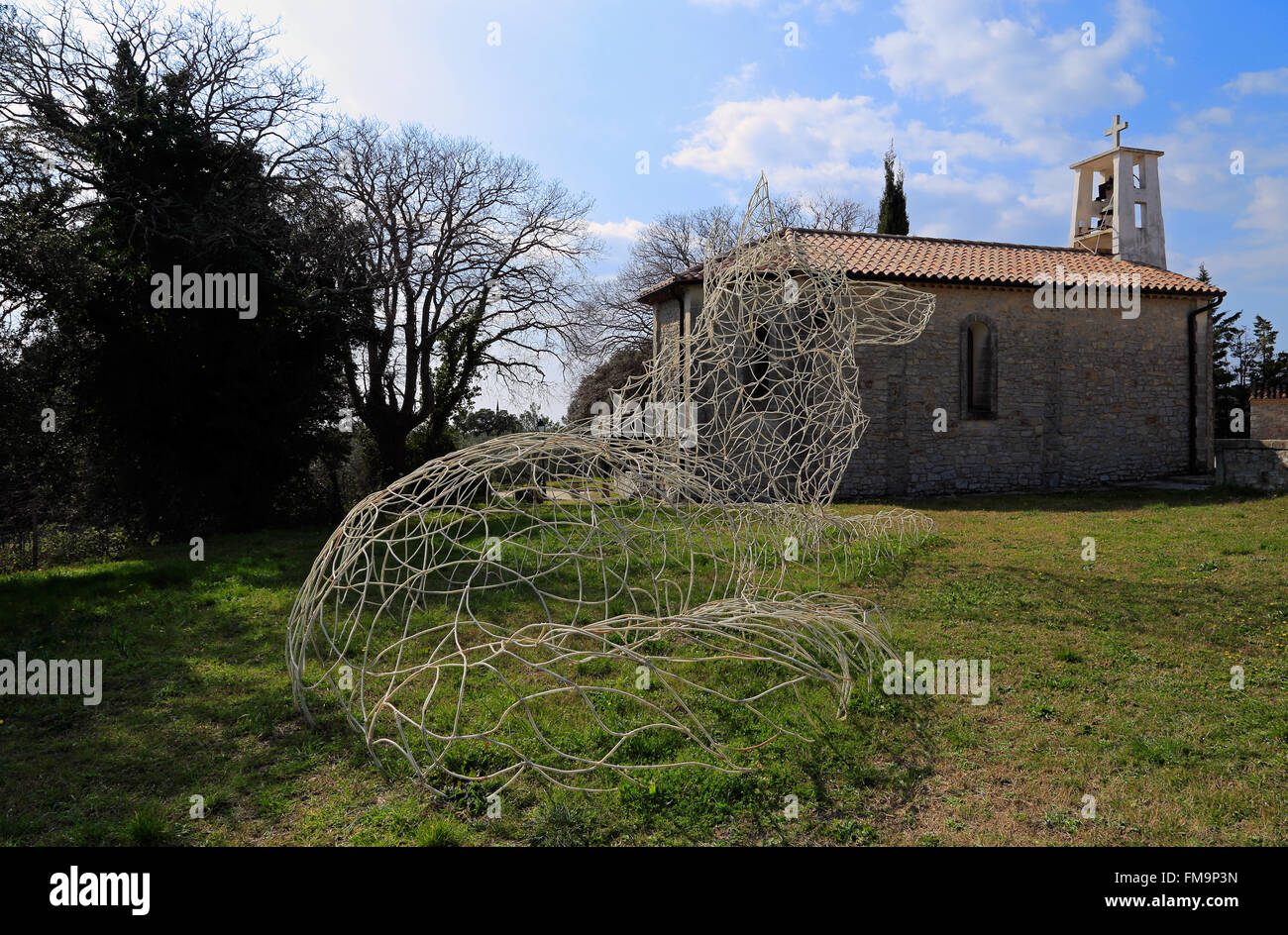 Cazevieille, Languedoc-Roussillon, Francia. Undicesimo Marzo 2016. La scultura e la chiesa del villaggio ai piedi del Pic Saint Loup nel tardo inverno. Foto Stock