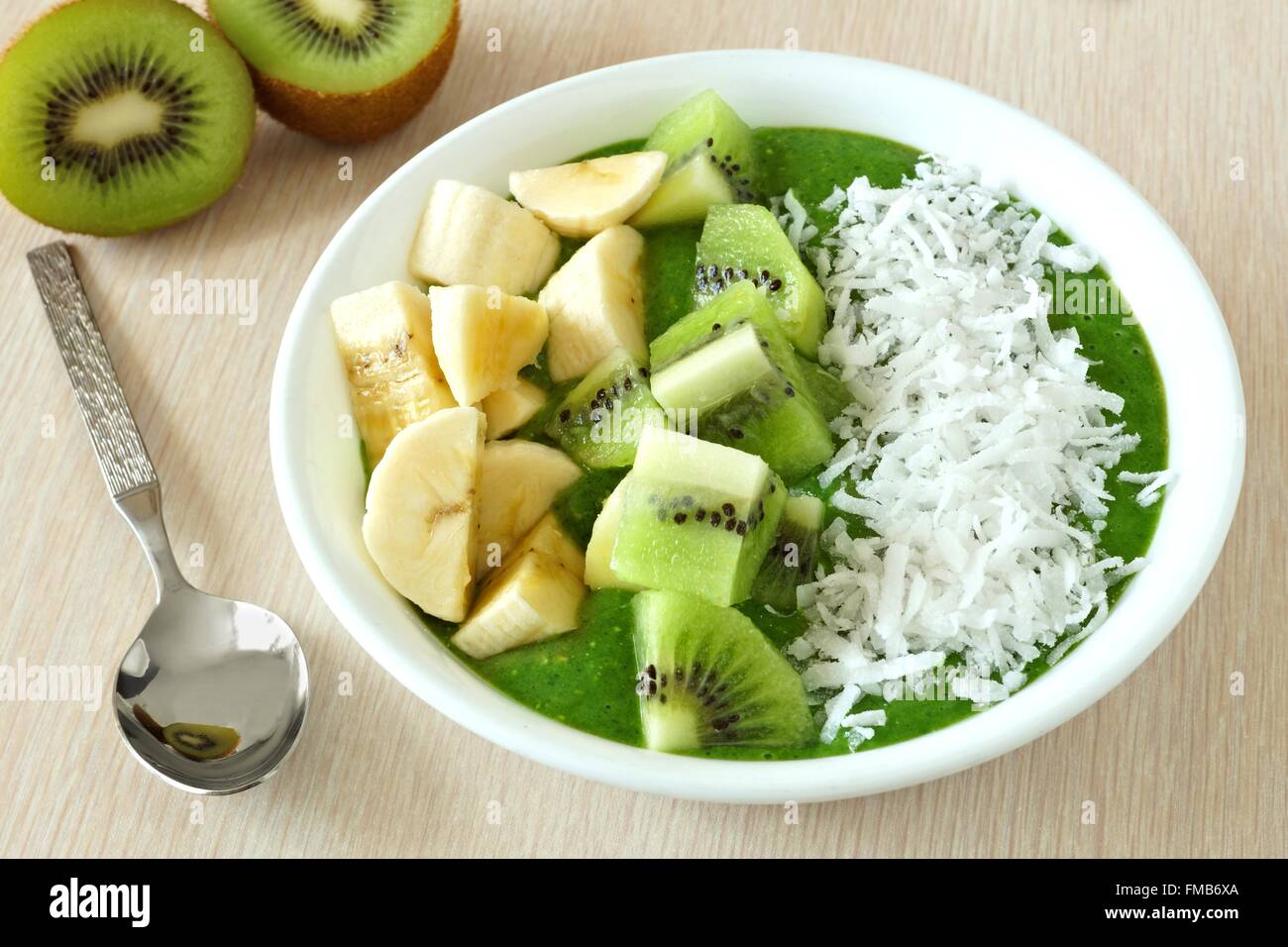 Frullato verde ciotola con le banane fresche kiwi e cocco con cucchiaio su un tavolo Foto Stock