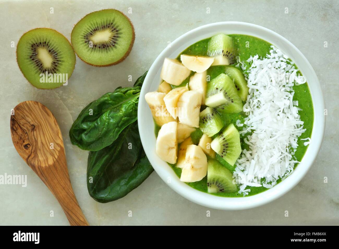 Frullato verde ciotola con spinaci, Banane, kiwi e cocco con cucchiaio su un marmo bianco sullo sfondo Foto Stock