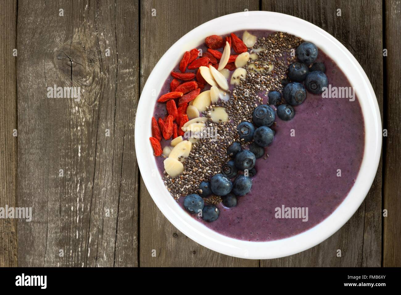 Un sano frullato mirtillo ciotola con super-alimenti contro un rustico sfondo di legno vecchio Foto Stock