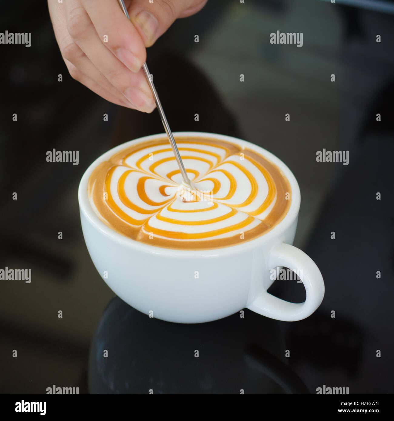 Barista decorare la superficie superiore del latte art caffè nella tazza bianca su sfondo nero Foto Stock