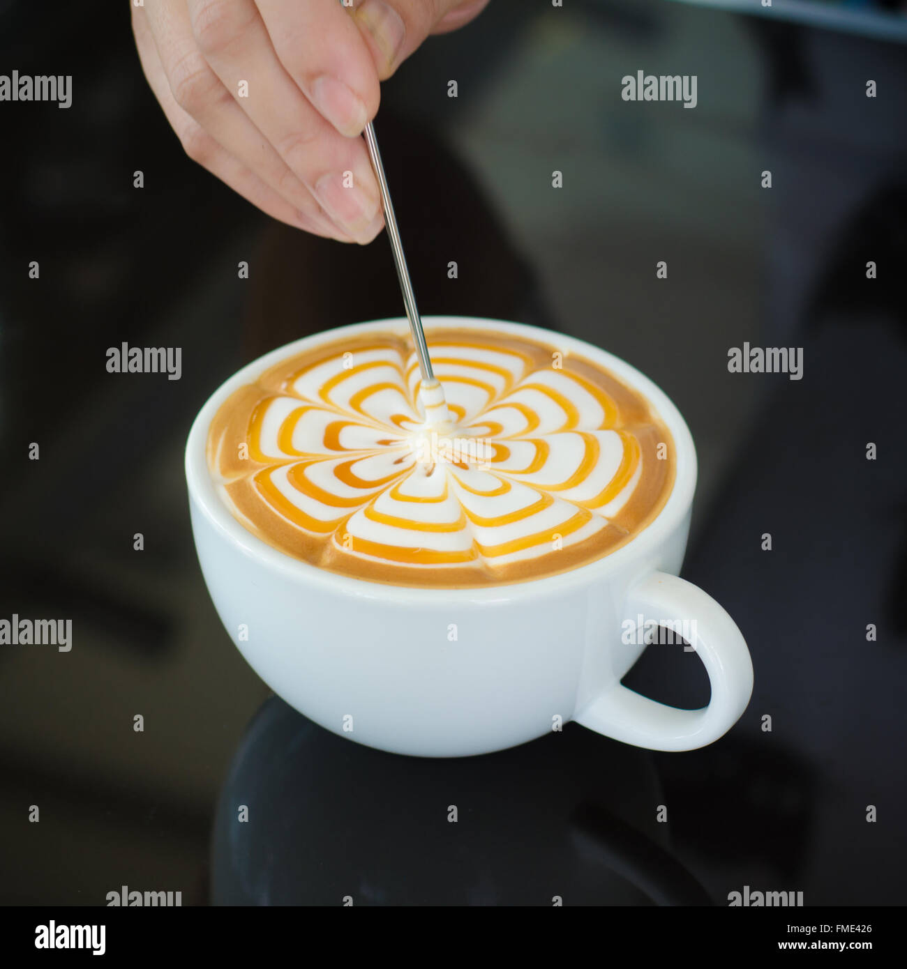 Barista decorare la superficie superiore del latte art caffè nella tazza bianca su sfondo nero Foto Stock