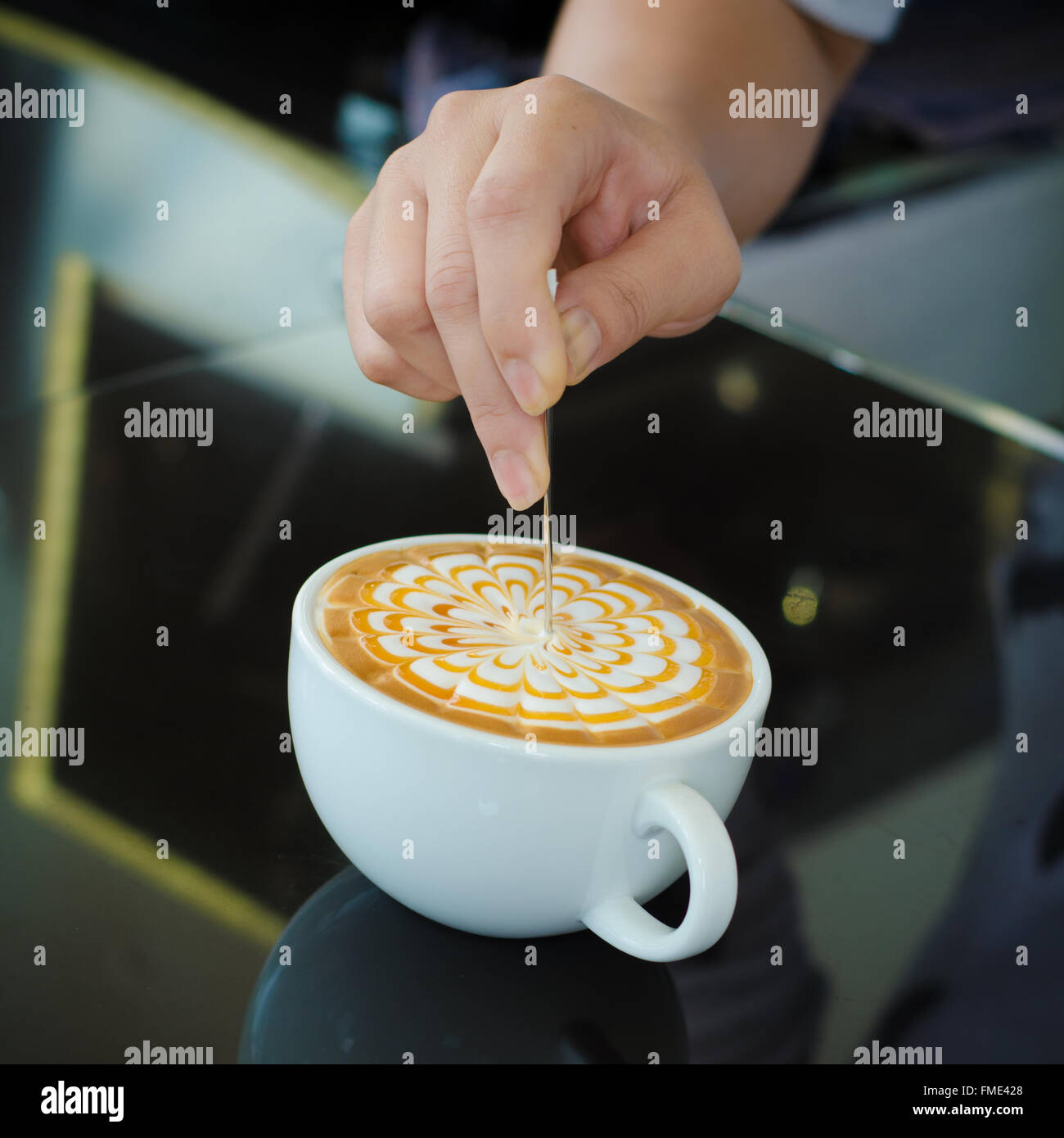 Barista decorare la superficie superiore del latte art caffè nella tazza bianca su sfondo nero Foto Stock