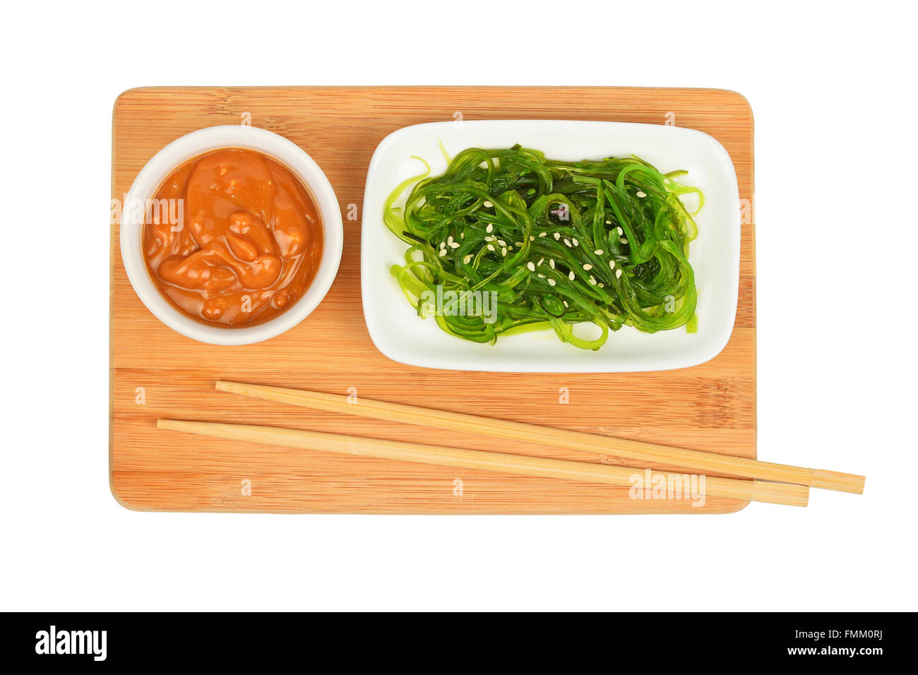 Porzione di verde asiatico marinato insalata di alghe marine in piccola piastra bianca con salsa di arachidi in bamboo tavoletta di legno con bacchette iso Foto Stock