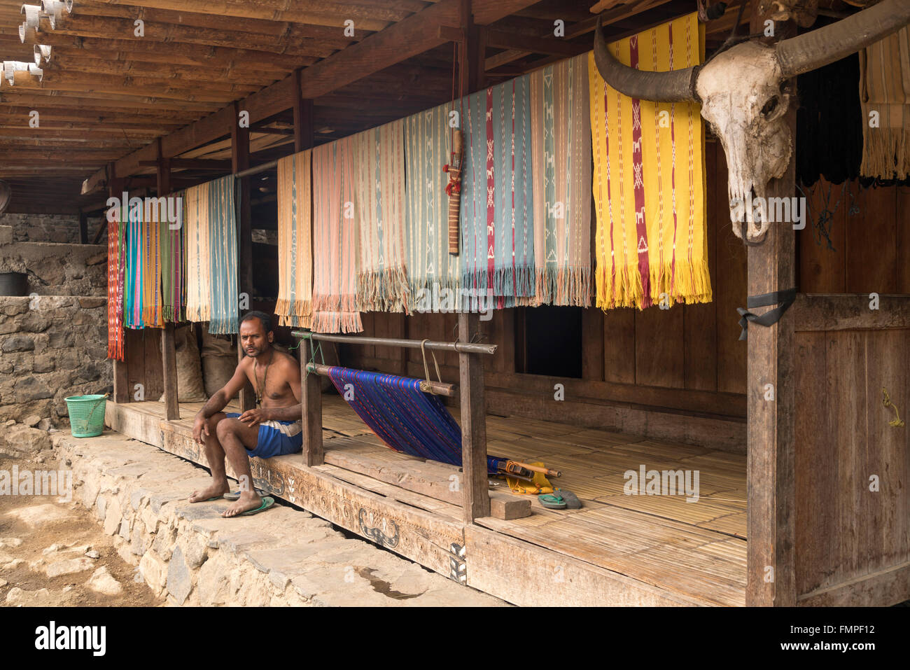 Ngada uomo seduto su un portico con tessuti ikat mostrando e corno di bufalo, villaggio tradizionale Bena, Bajawa, sull isola di Flores, Indonesia Foto Stock