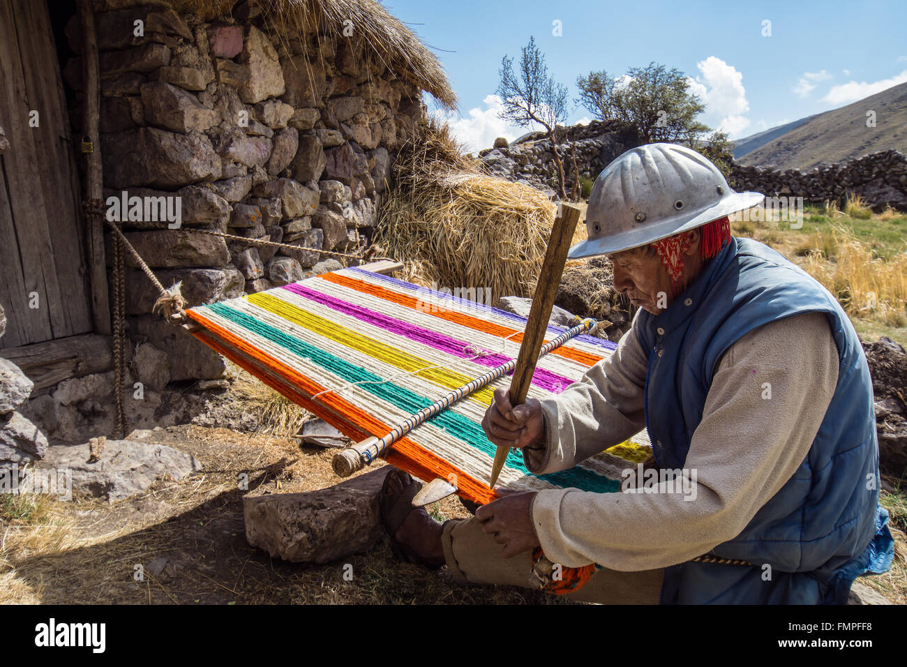 Vecchio indio uomo con casco tessitura di un coloratissimo tappeto con un semplice telaio, in Cusco, Perù Foto Stock