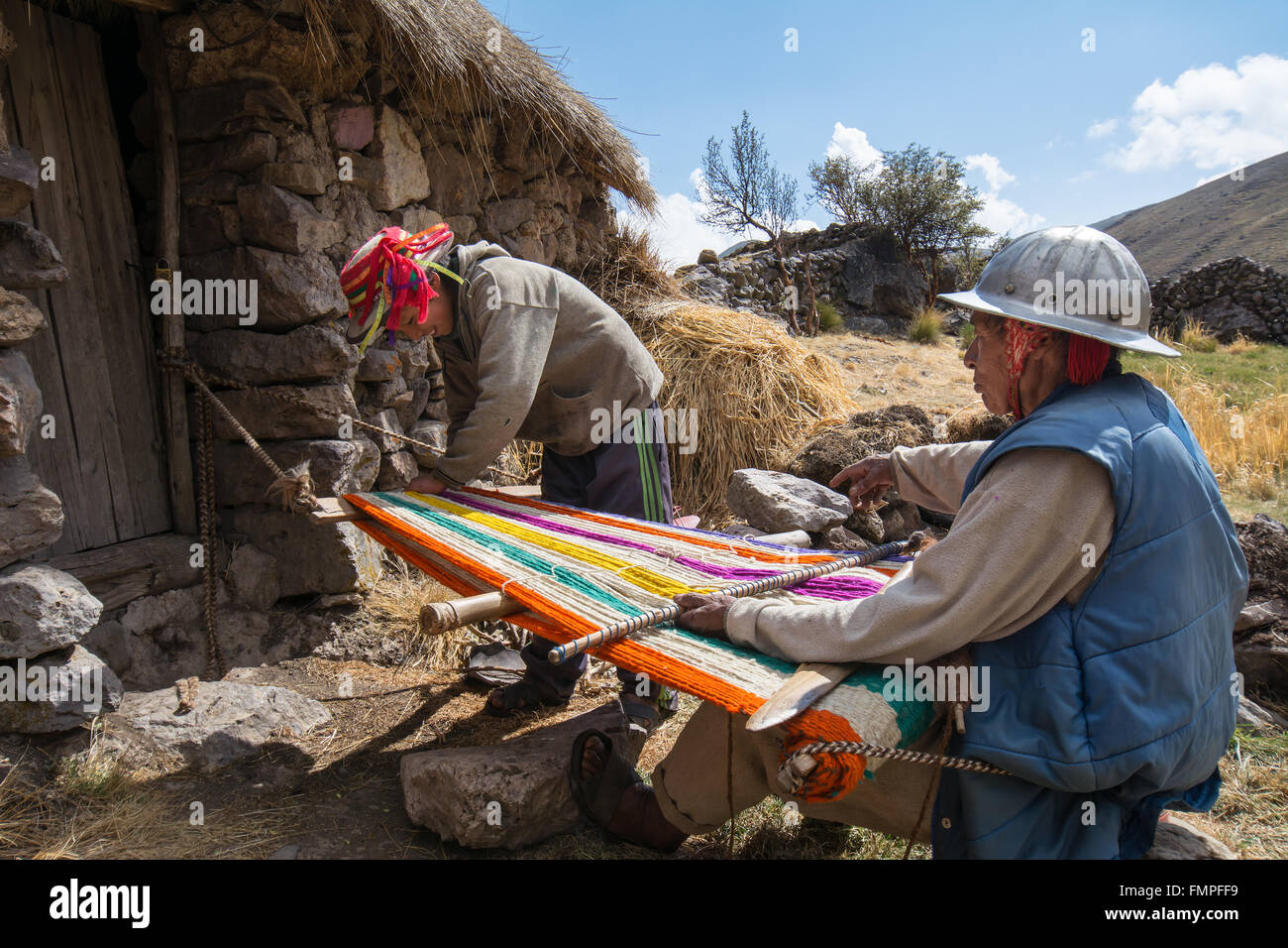 Vecchio indio uomo con casco tessitura di un coloratissimo tappeto con un semplice telaio, in Cusco, Perù Foto Stock