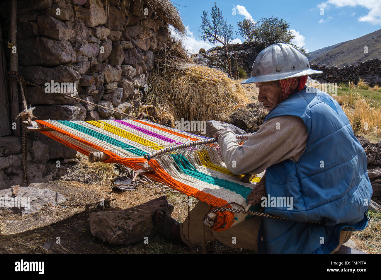 Vecchio indio uomo con casco tessitura di un coloratissimo tappeto con un semplice telaio, in Cusco, Perù Foto Stock