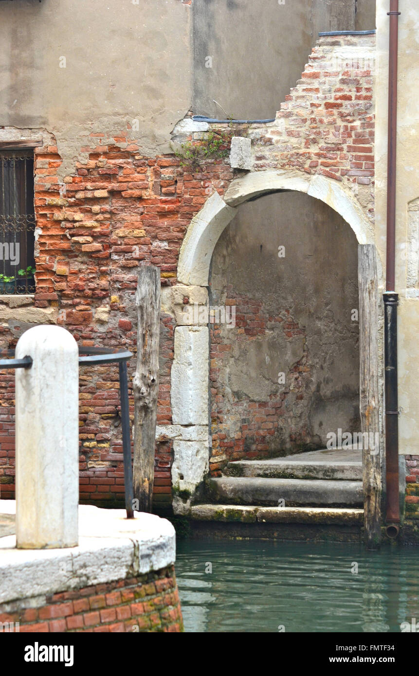 Uno sbriciolamento archway a Venezia. Essa si apre su di un canale ed è incorniciato da vecchio sbriciolamento mattoni. Un bianco post è in primo piano. Foto Stock