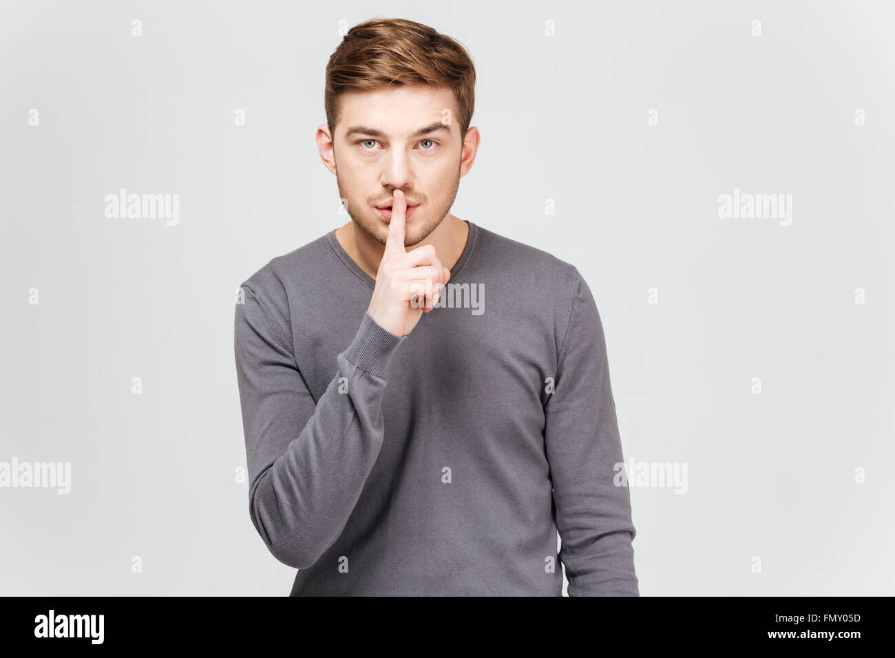 Bel giovane uomo in grigio pullover che mostra il silenzio gesto su sfondo bianco Foto Stock