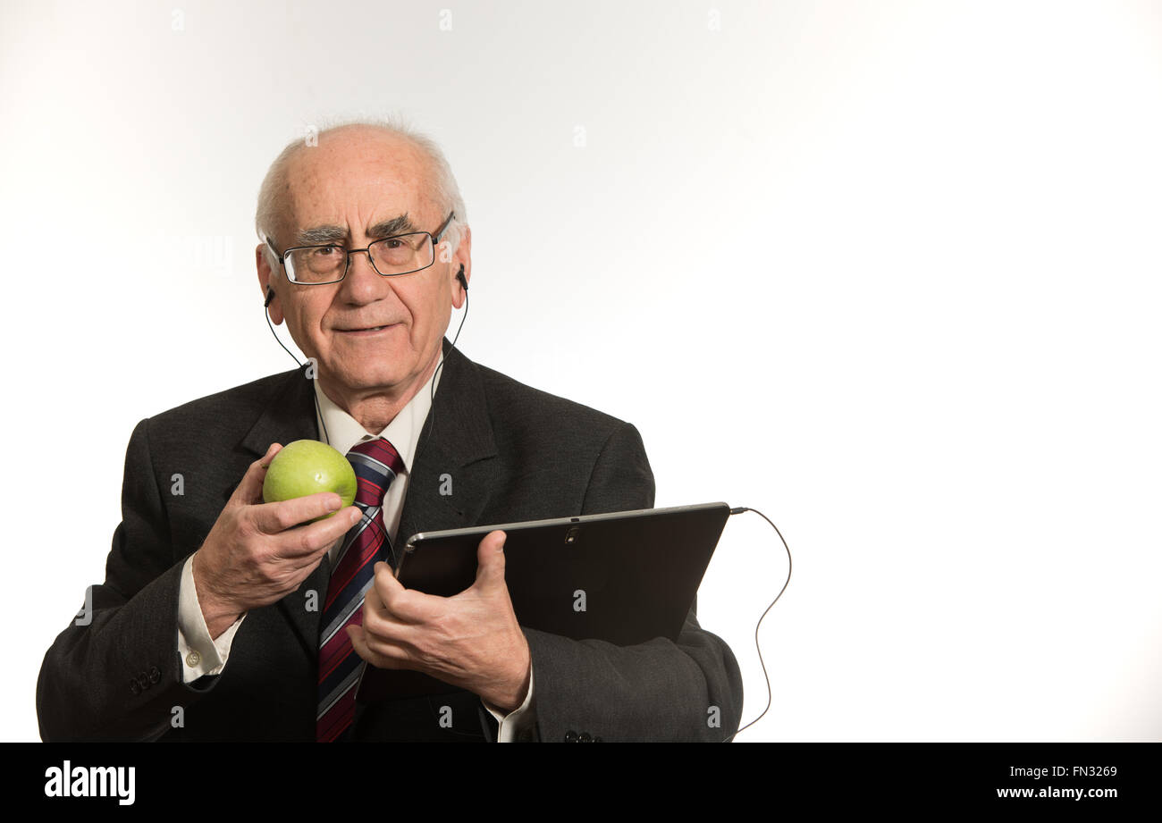 Vecchio imprenditore senior lavora con nero computer tablet, indossando il business suit, mangiare apple Foto Stock Vecchio imprenditore senior lavora con nero computer tablet, indossando il business suit, mangiare apple Foto Stock