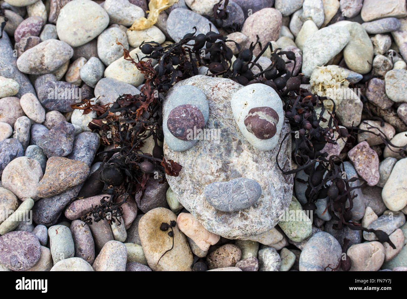 Faccia realizzato da ciottoli e le alghe sulla spiaggia Foto Stock