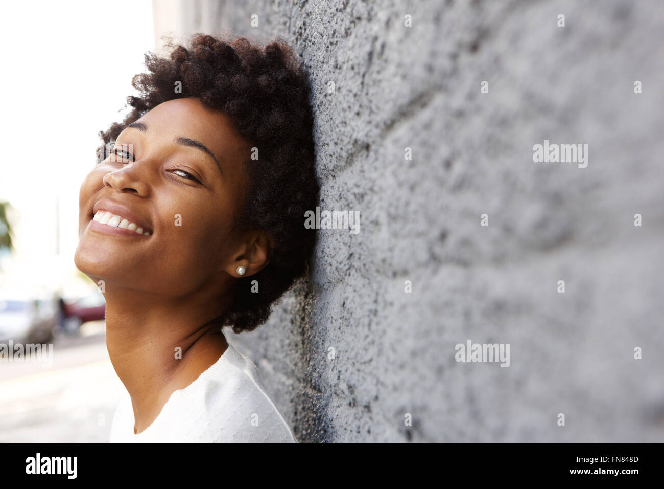 Closeup ritratto di felice giovane donna africana appoggiata ad una parete esterna con copia spazio nella parte anteriore Foto Stock