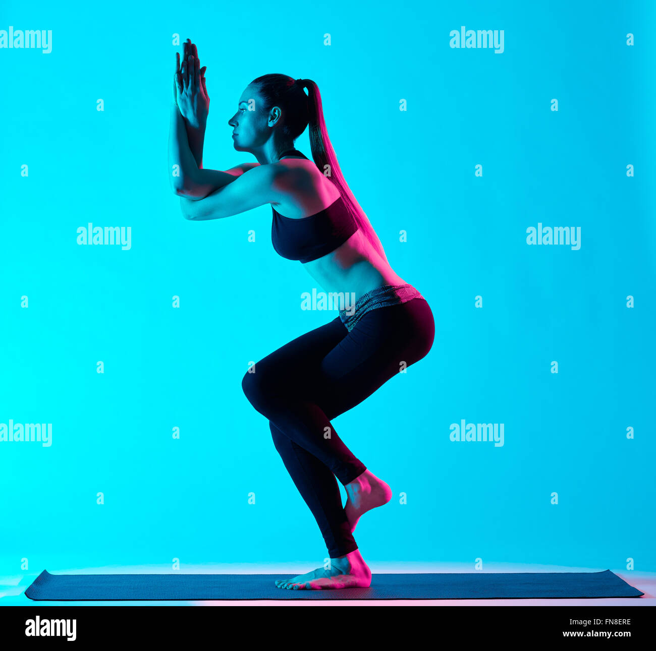 Una donna caucasica esercizio Garudasana posizione dell'aquila esercizi di yoga in silhouette studio isolato su sfondo blu Foto Stock