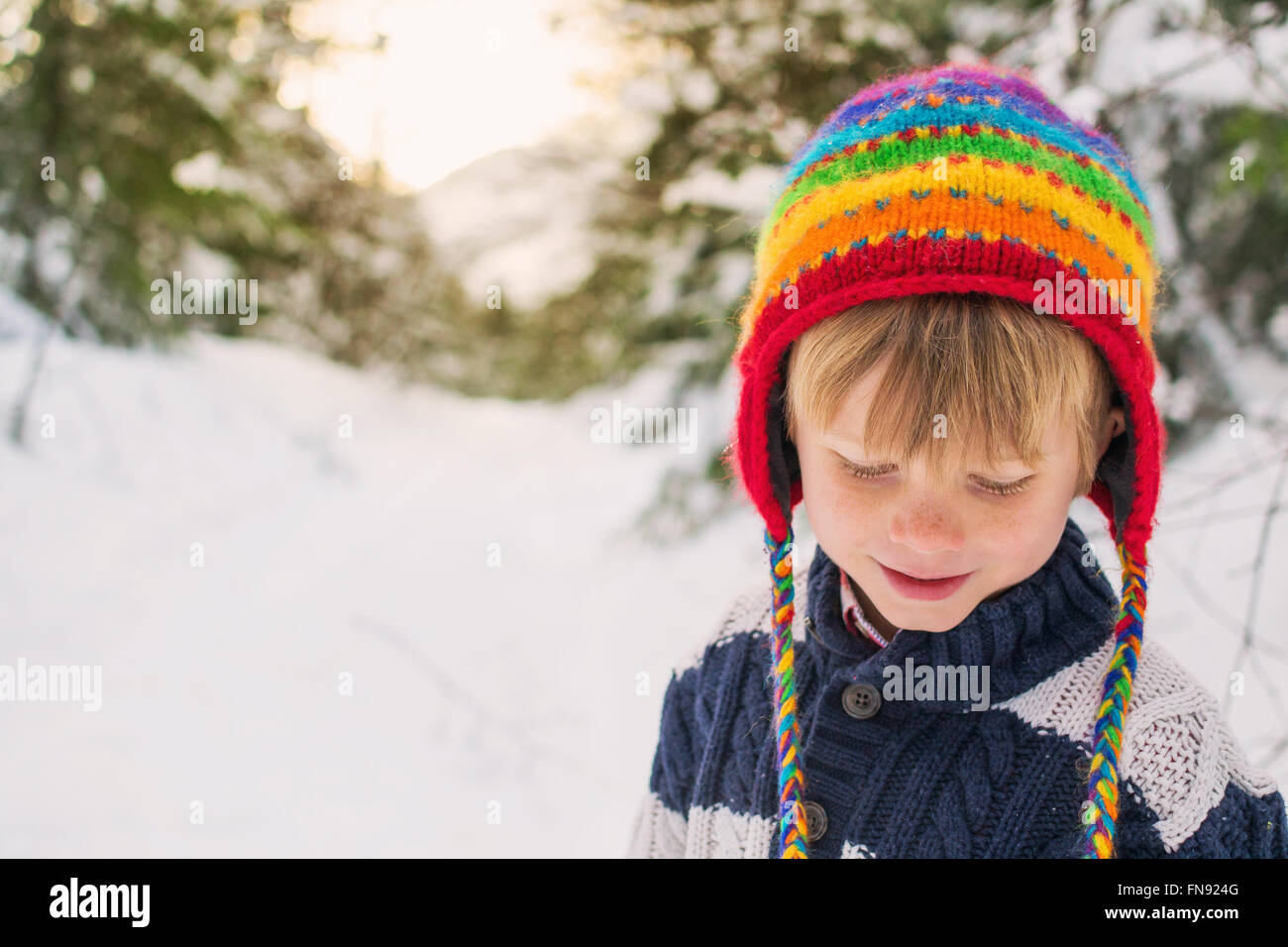 Ragazzo in cappello multicolore nella neve guardando giù Foto Stock