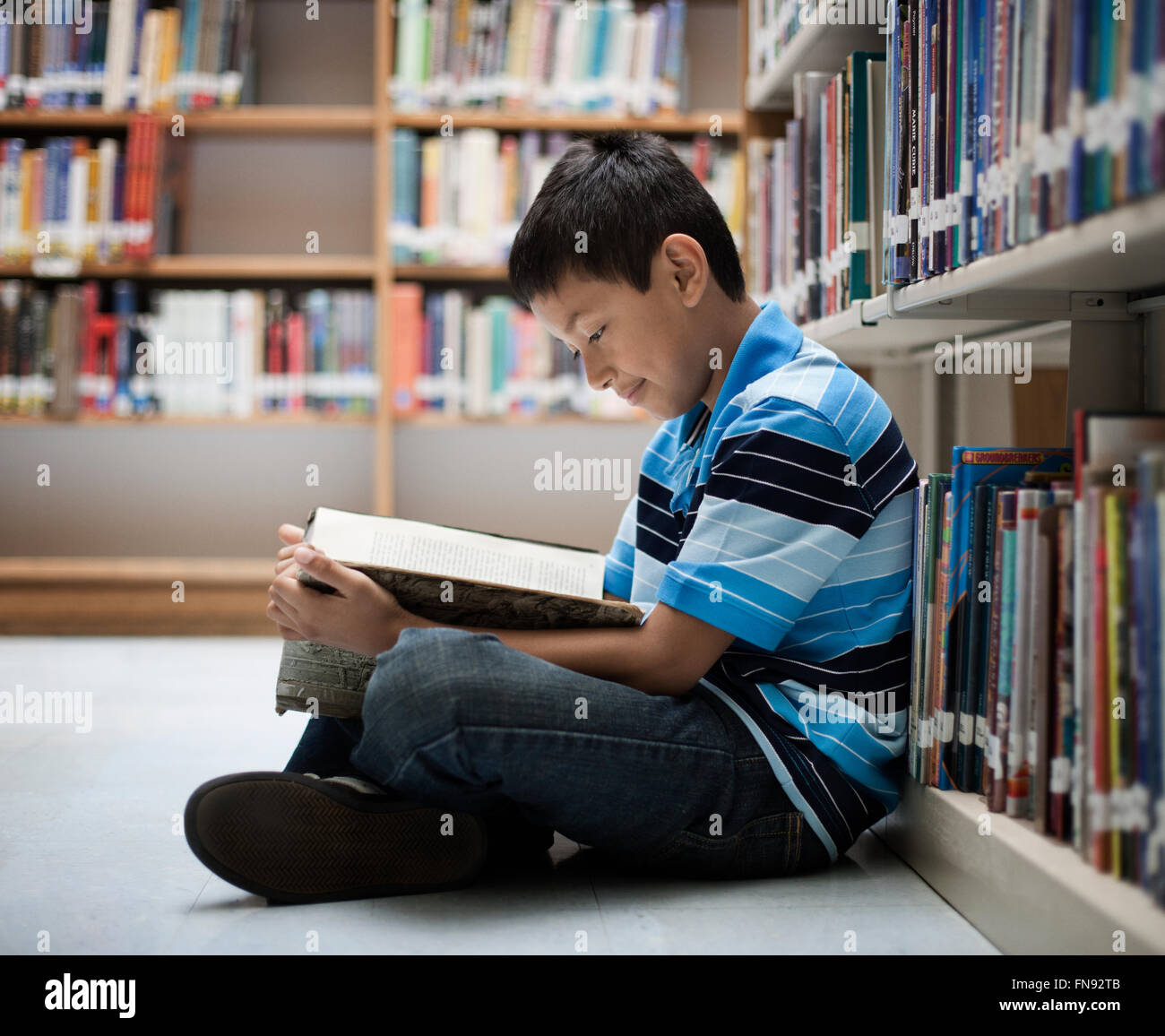 Un ragazzo seduto sul pavimento in una libreria la lettura di un libro. Foto Stock
