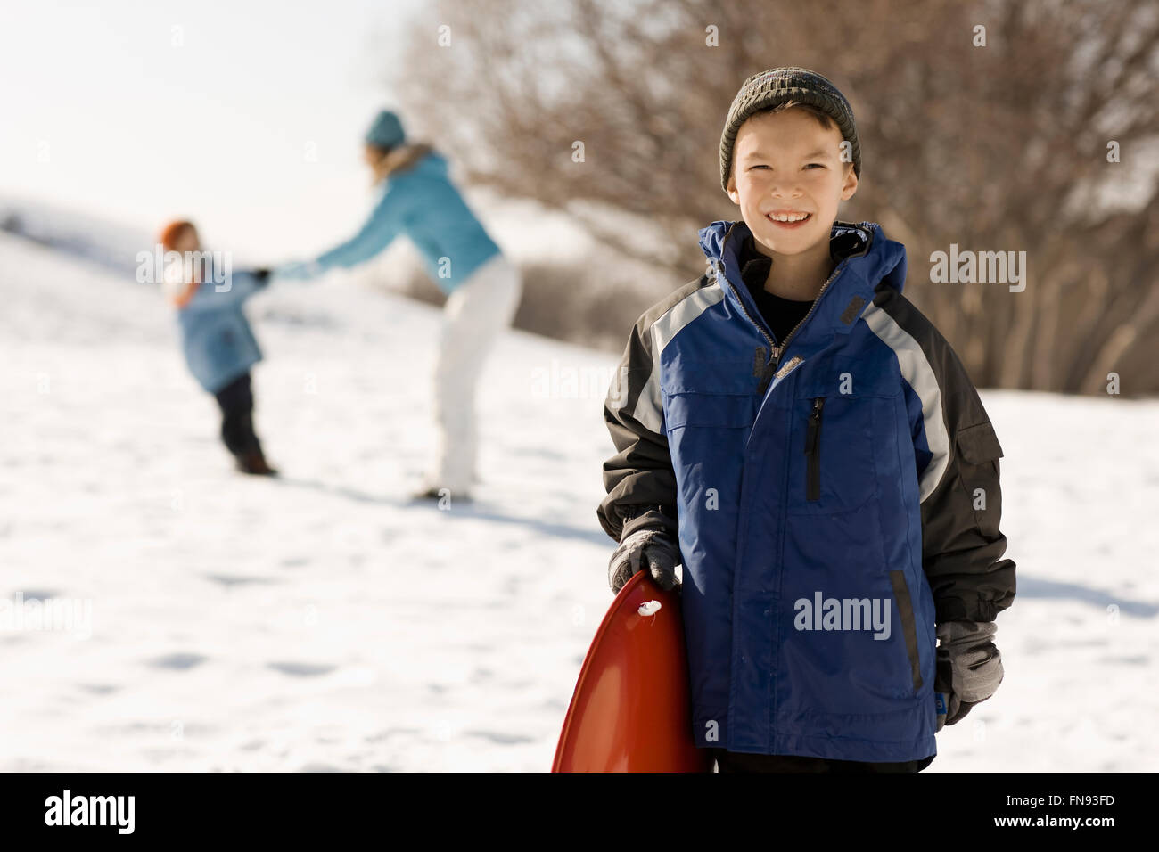 Un ragazzo in possesso di una slitta nella neve e una madre e un bambino dietro di lui. Foto Stock