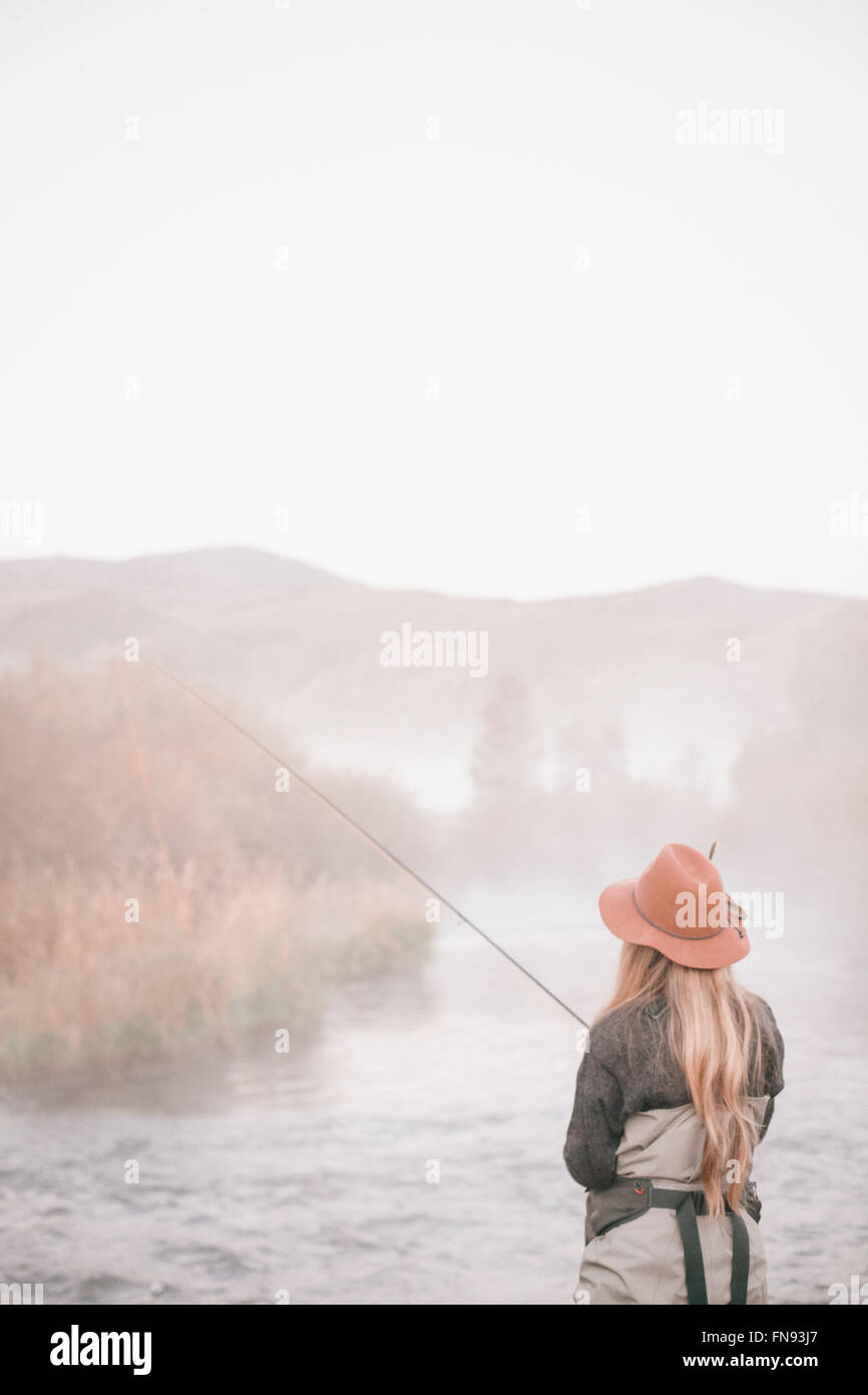 Un pescatore, una donna in piedi sulle rive di un fiume, pesca a mosca. Foto Stock