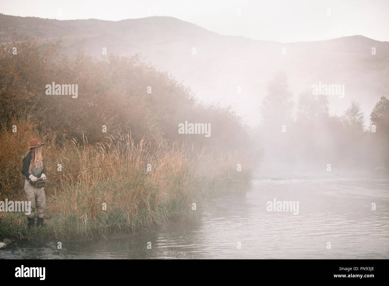 Una donna la pesca, in piedi sulla riva del fiume. Mist rising dall'acqua. Foto Stock