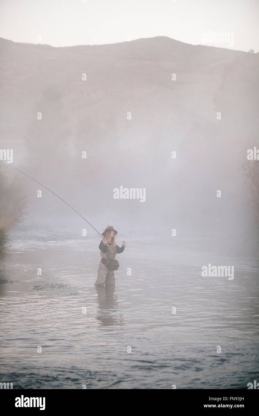 Una donna pescatore pesca a mosca, in piedi di waders a coscia in acque profonde. Foto Stock