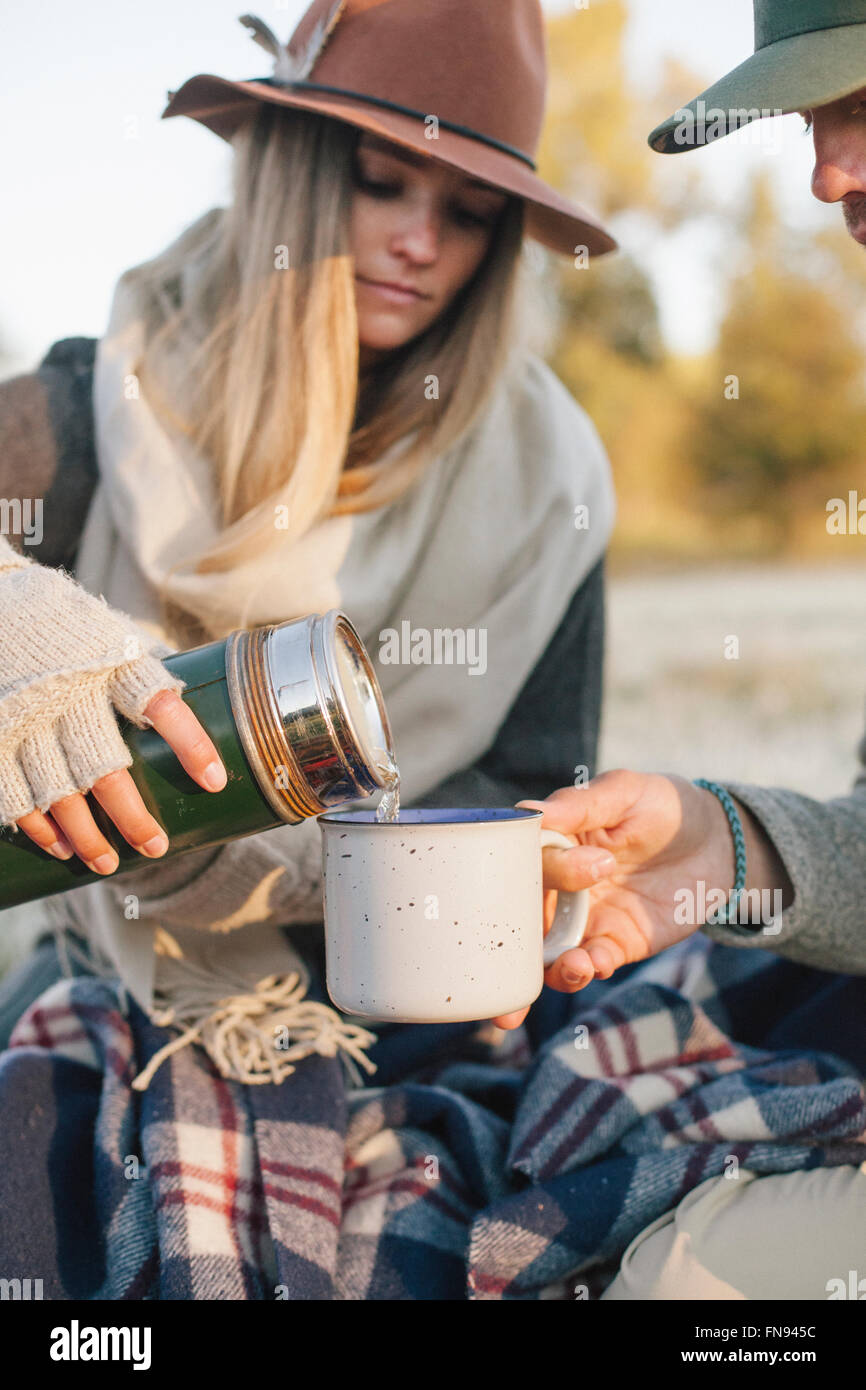 Una donna versando una bevanda calda da una beuta da vuoto in un bicchiere su un picnic d'inverno. Foto Stock