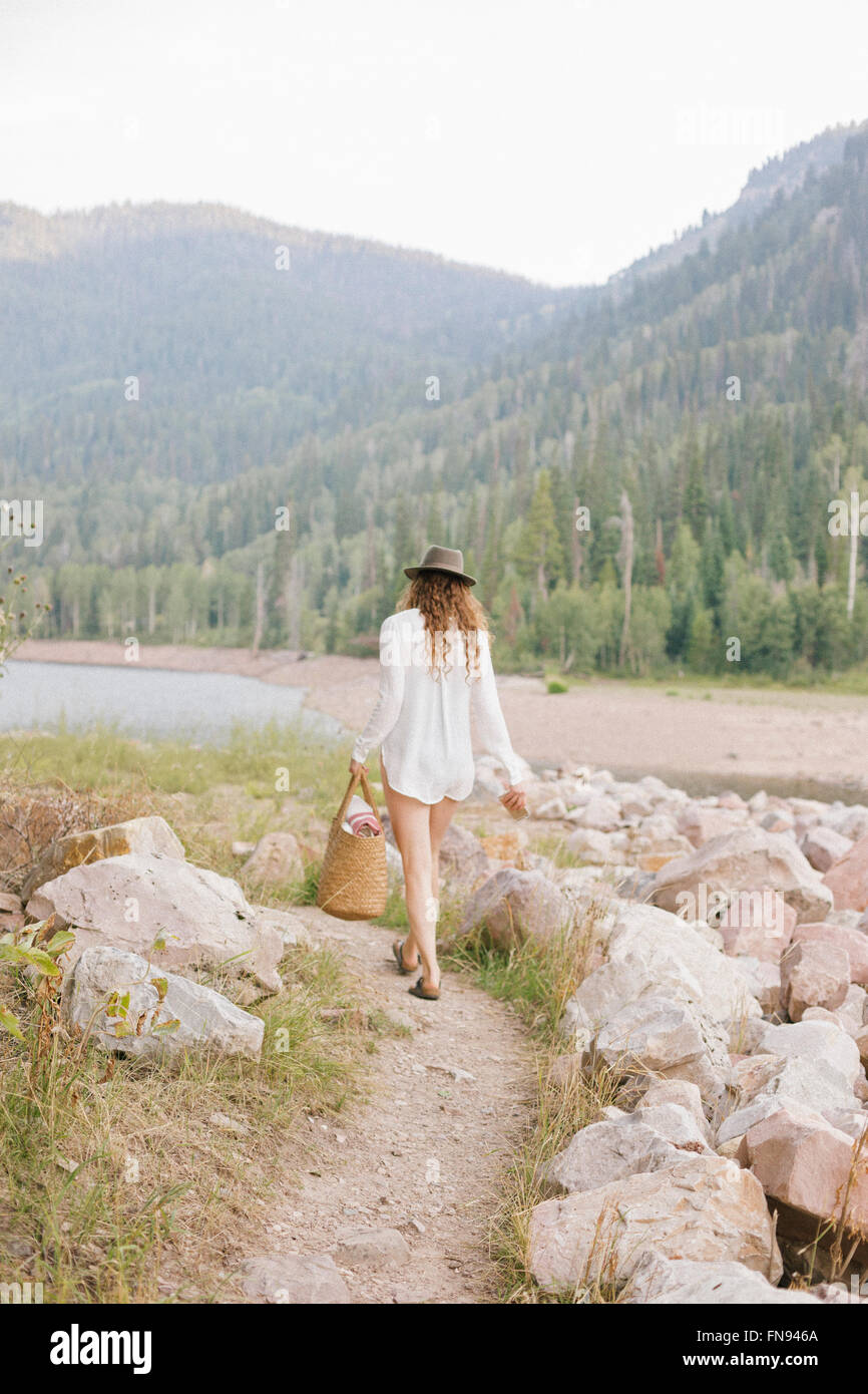 Una donna in un cappello e una camicia bianca con un cestello, sulle sponde di un lago di montagna. Foto Stock