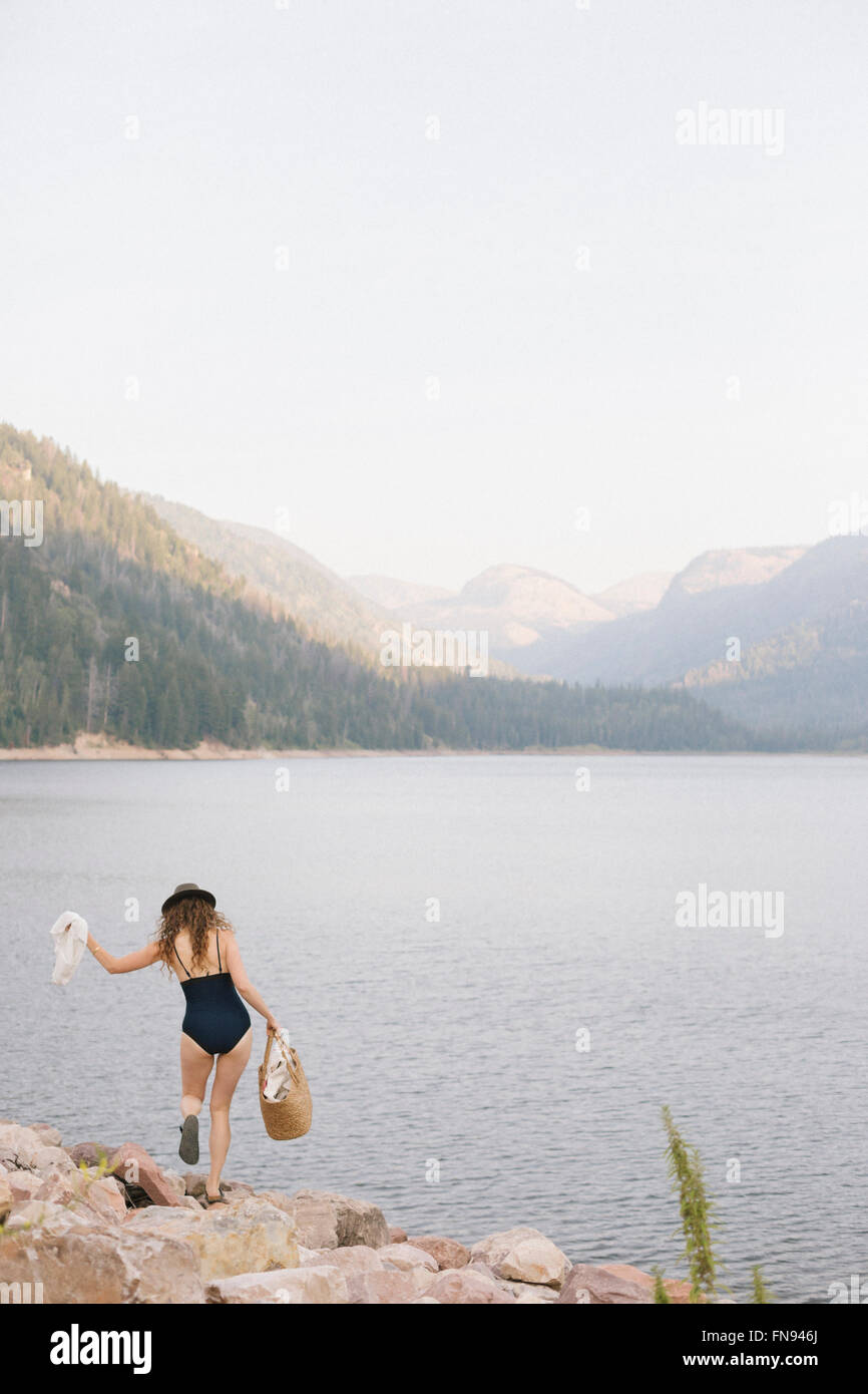 Una donna in costume da bagno portando un cesto lungo la riva di un lago di montagna. Foto Stock
