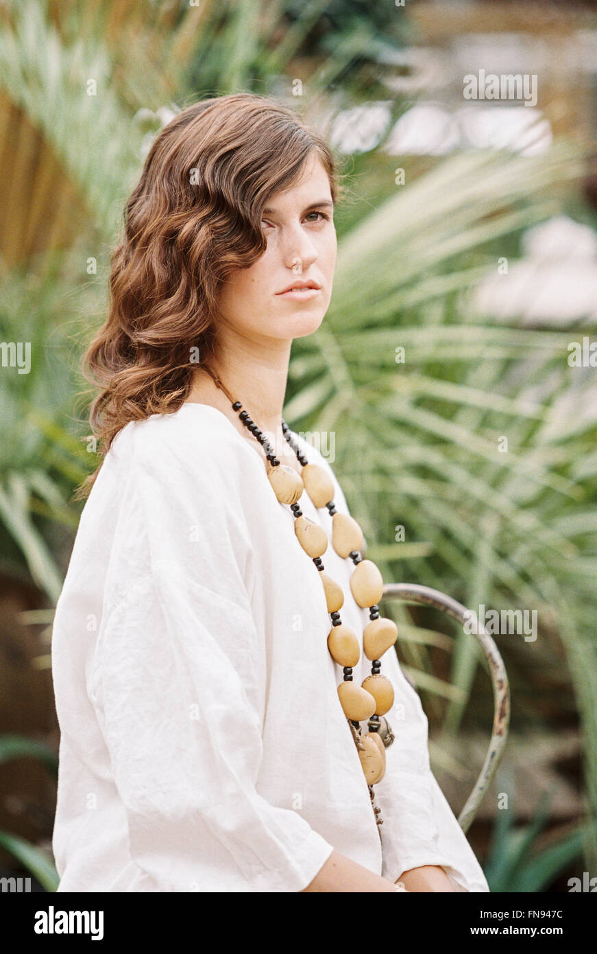 Una giovane donna con ricci capelli marroni che indossa una camicia bianca e collana. Foto Stock