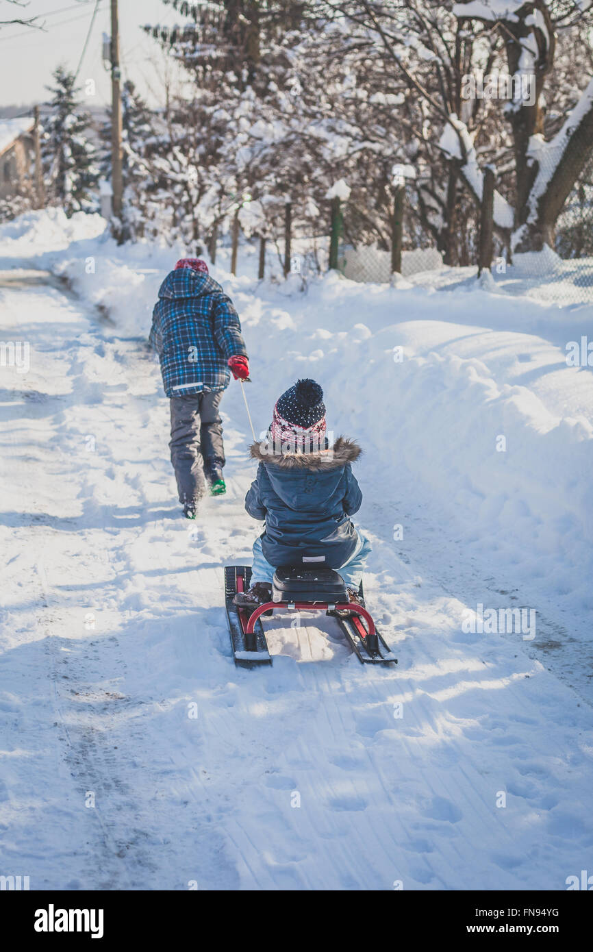 Ragazzo tirando la sorella su una slitta nella neve Foto Stock