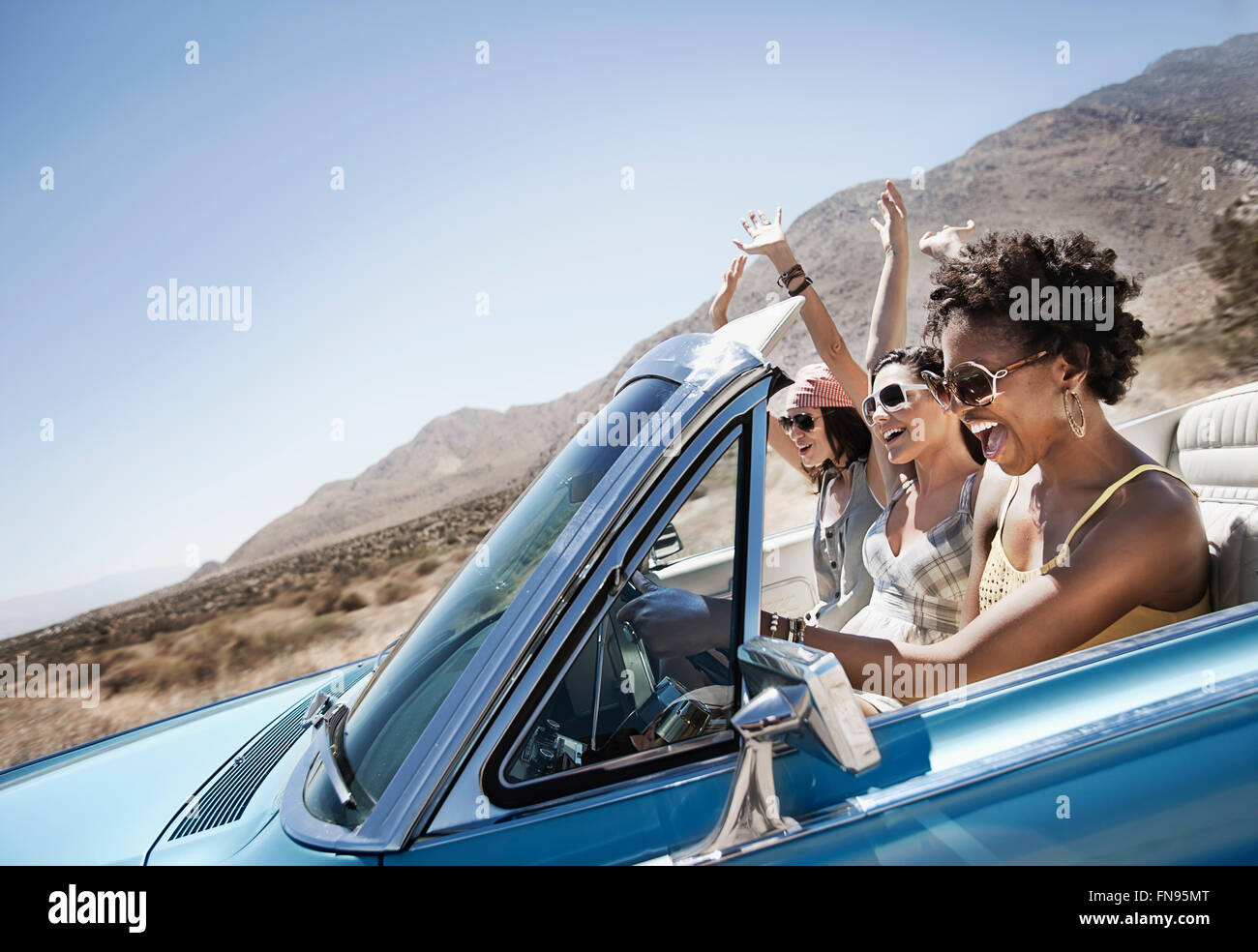Tre giovani in un colore blu pallido autovettura convertibile, guida su strada aperta attraverso una piatta pianura a secco, Foto Stock