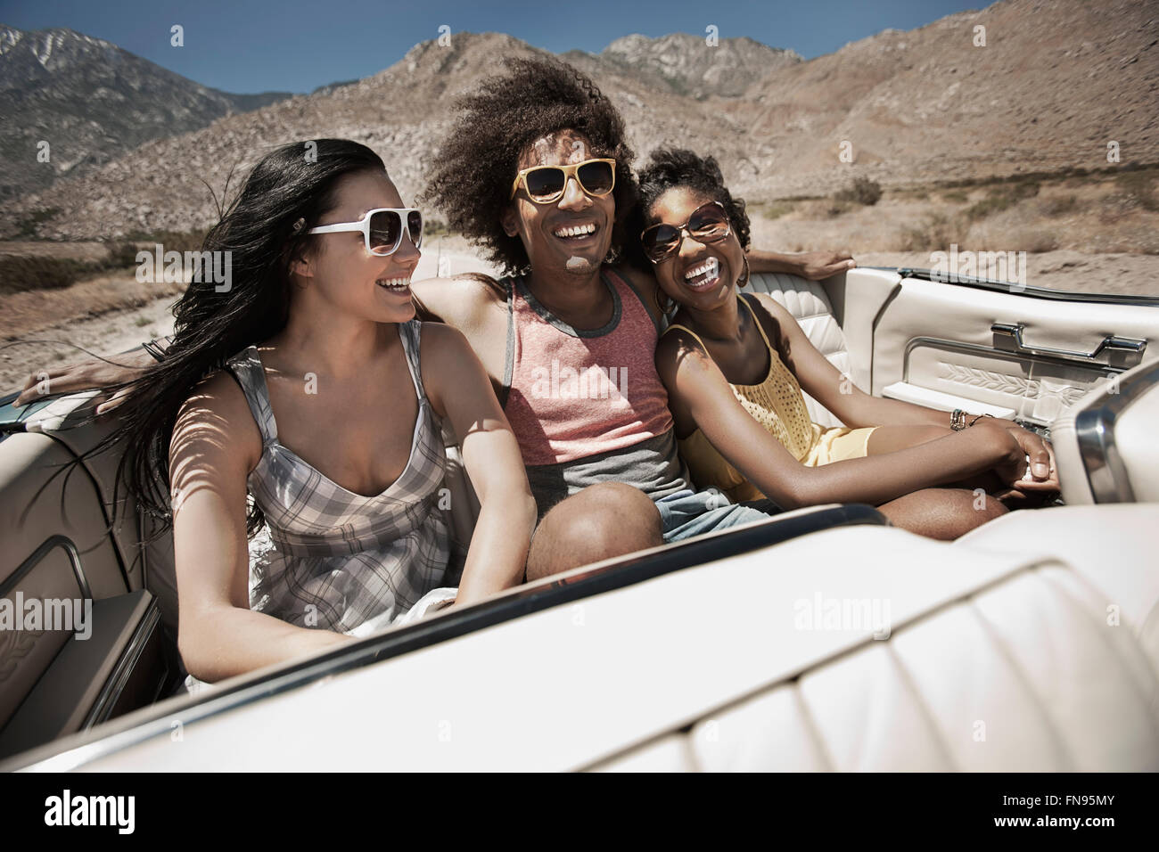 Tre giovani in un colore blu pallido autovettura convertibile, guida su strada aperta attraverso una piatta pianura a secco, Foto Stock