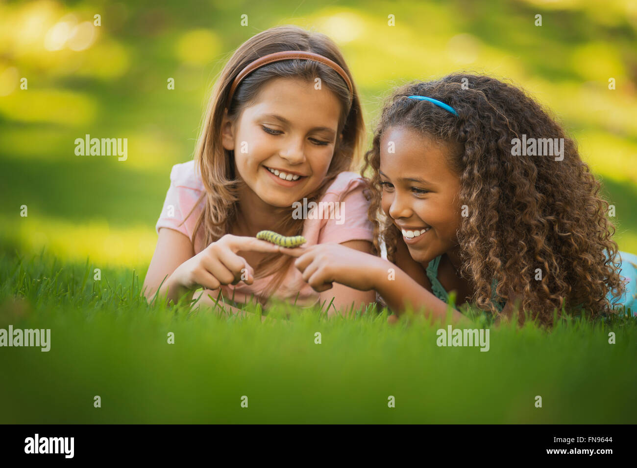Due ragazze sdraiati sull'erba, una holding di un bruco verde sul suo dito. Foto Stock