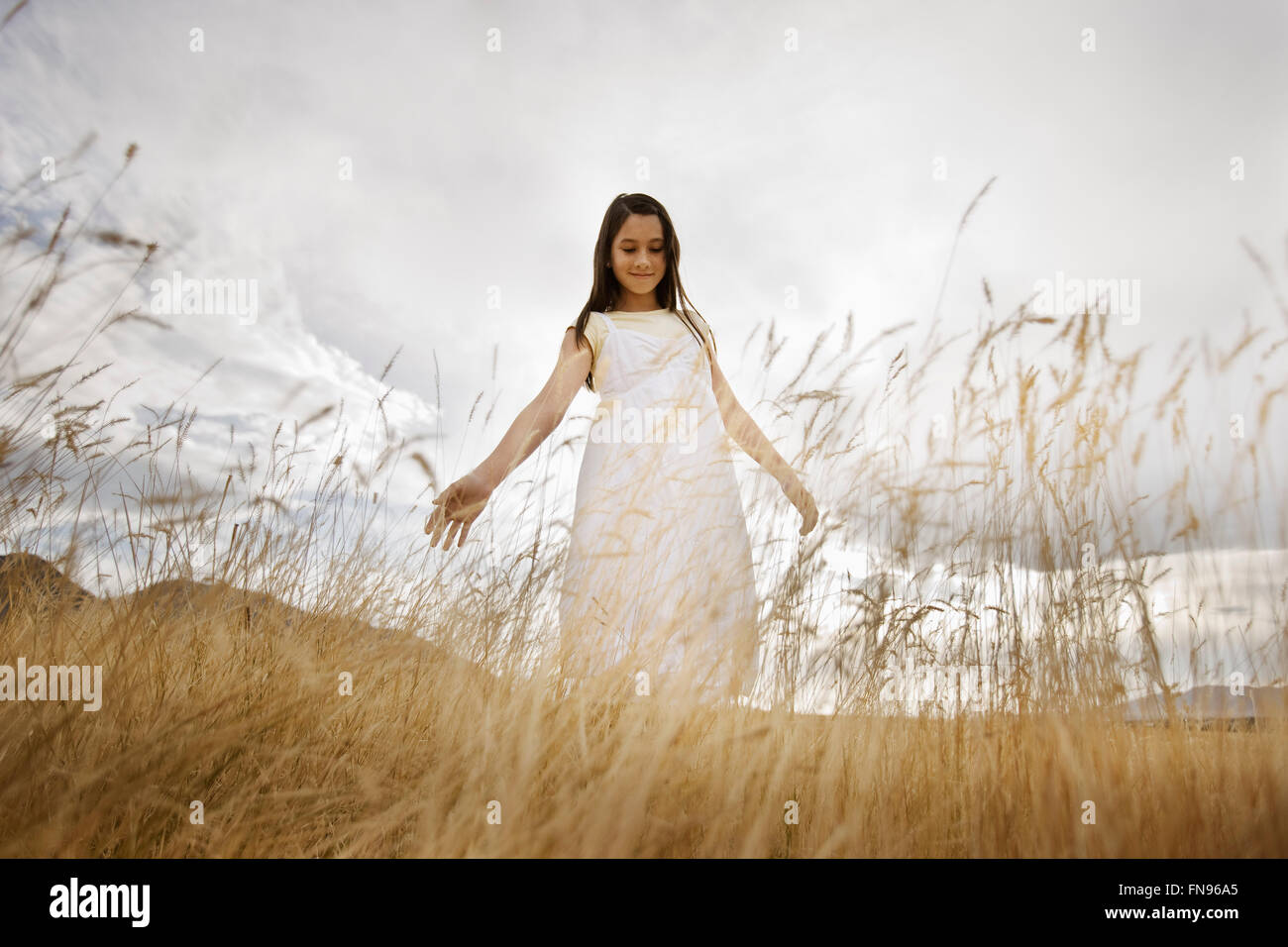 Una ragazza in un abito bianco in erba lunga, guardando in giù con le braccia ha tenuto fuori dal suo lato. Foto Stock