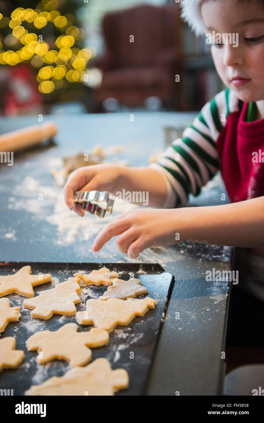 Un ragazzo in un cappello da Babbo Natale rendendo i biscotti di Natale, ritagliando forme. Foto Stock