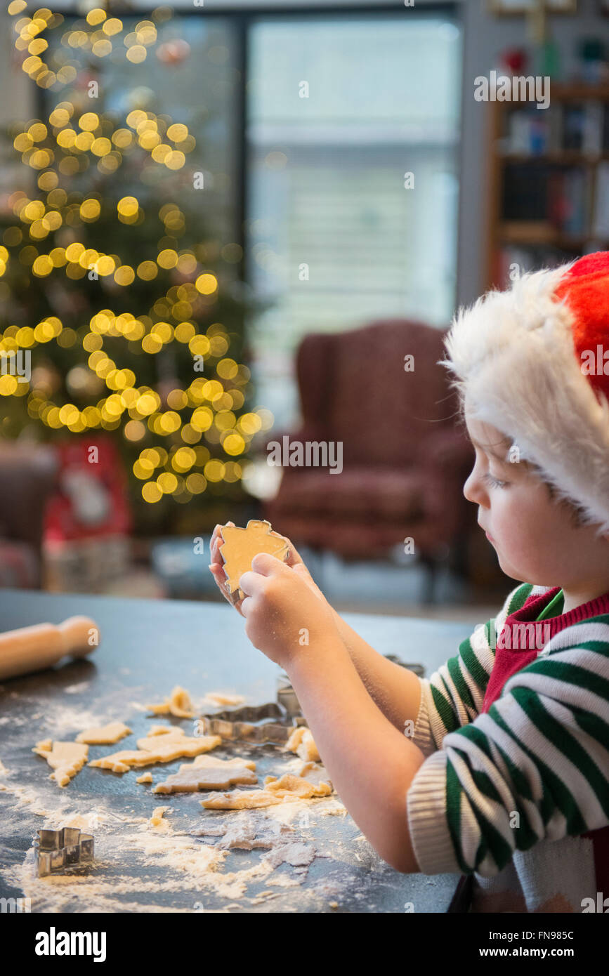 Un ragazzo in un cappello da Babbo Natale rendendo i biscotti di Natale, ritagliando forme. Foto Stock