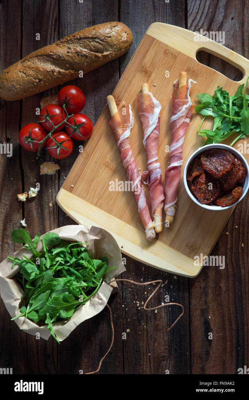Grissini avvolti nel prosciutto di Parma con pomodorini, rucola e pane Foto Stock