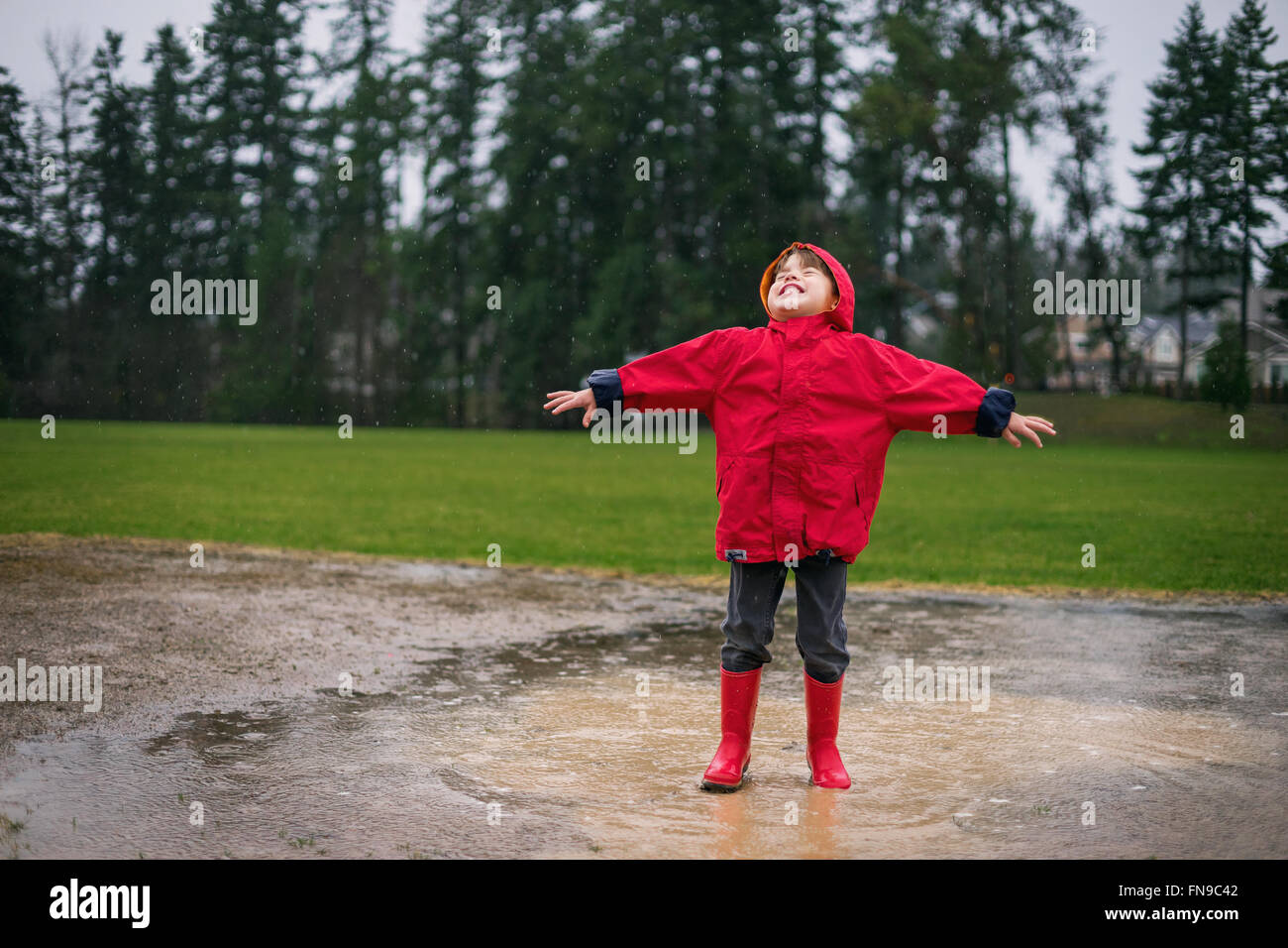 Giovane ragazzo in piedi in una pozza di pioggia con le braccia aperte Foto Stock