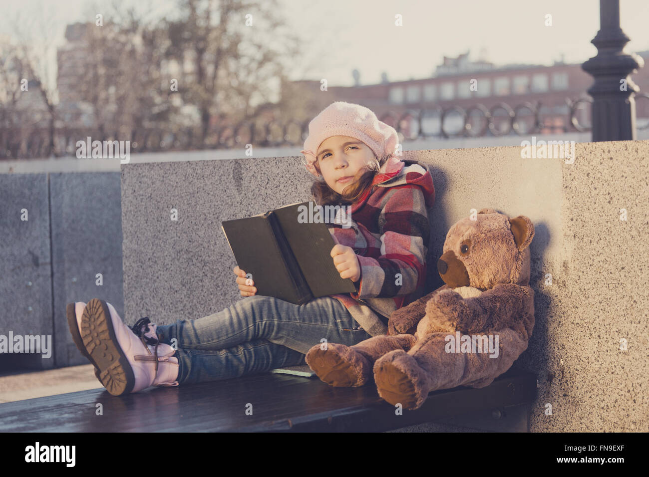 Bambina si siede su una panchina e legge il libro di un giocattolo bear.Elaborazione: tonificante e in colori caldi Foto Stock