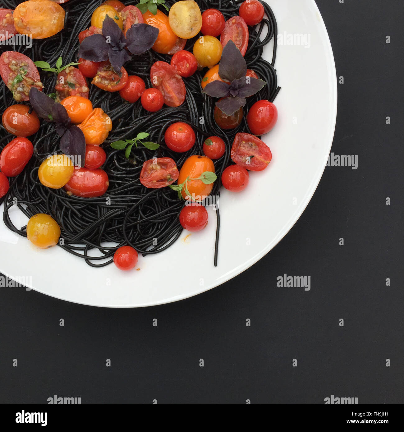 Pasta di colore nero con pomodorini e basilico Foto Stock