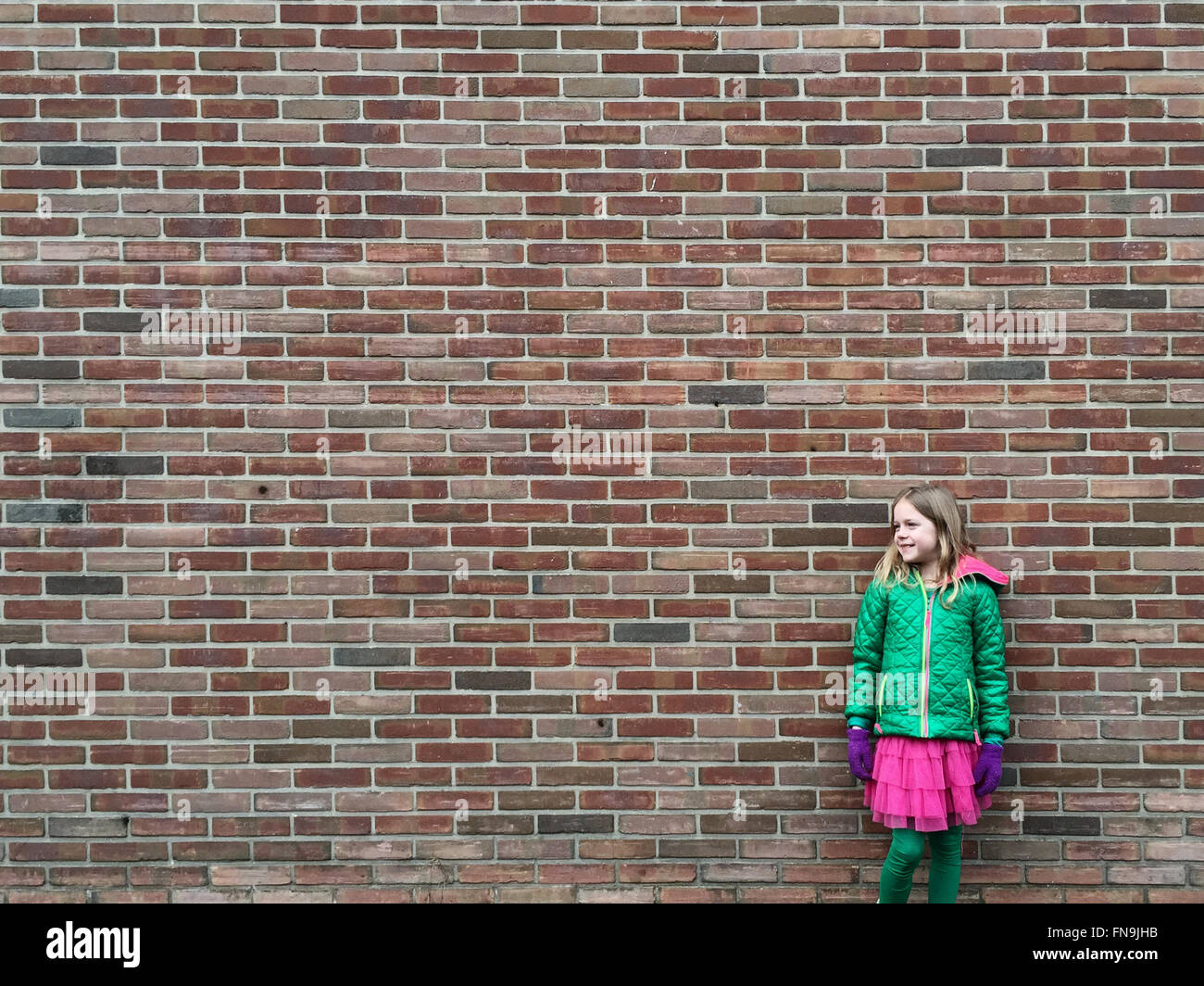 Ragazza sorridente in piedi di fronte a un muro di mattoni Foto Stock