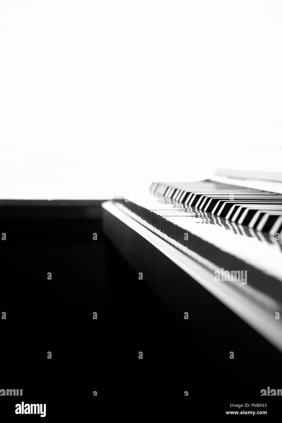 In bianco e nero il fuoco selettivo tastiera di pianoforte sparato da un angolo basso e retroilluminato con uno sfondo bianco Foto Stock