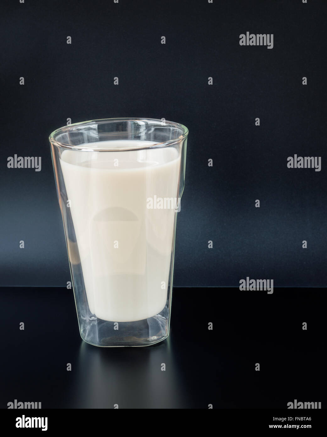 Latte vegetale in una doppia parete isolata bicchiere con su una tavola nera contro uno sfondo blu scuro Foto Stock