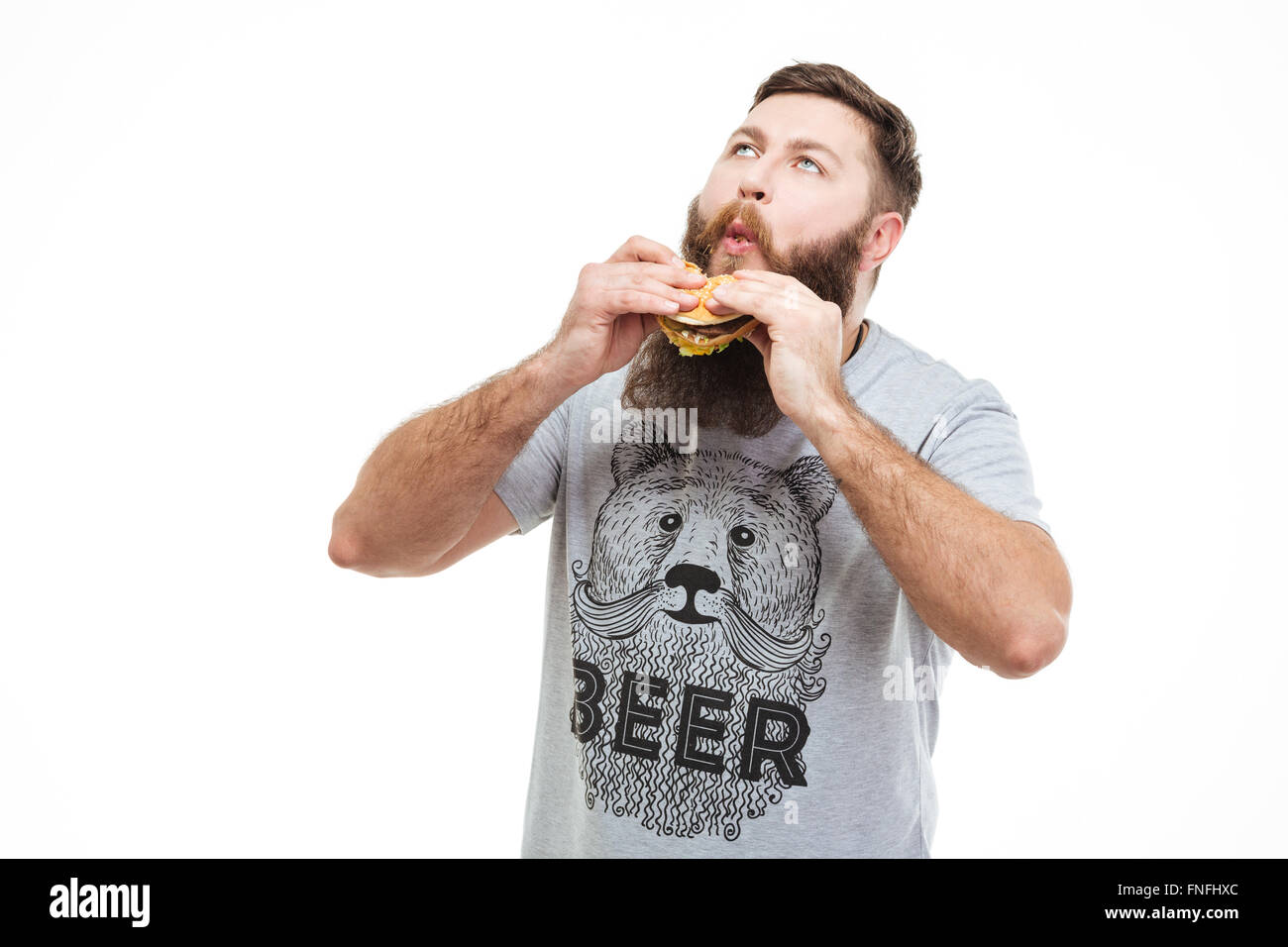 Emozionato uomo bello con la barba di mangiare hamburger e godendo su sfondo bianco Foto Stock
