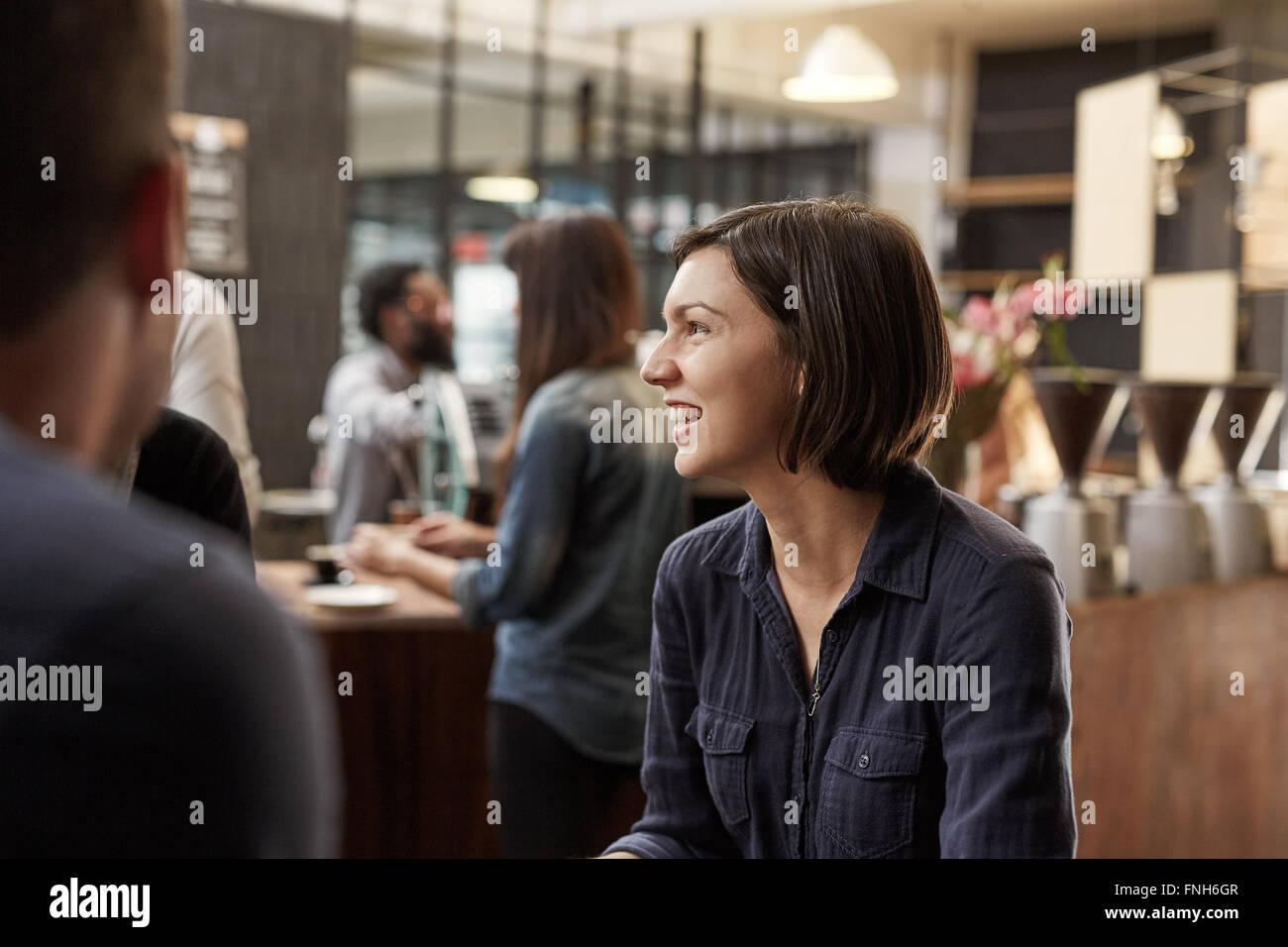 Brunette donna sorridente e guardando lontano in un occupato cafè Foto Stock