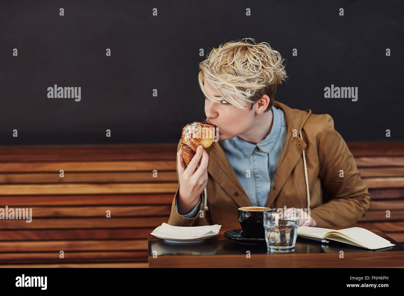 Giovane donna prendendo morso di brioche in un moderno cafe Foto Stock