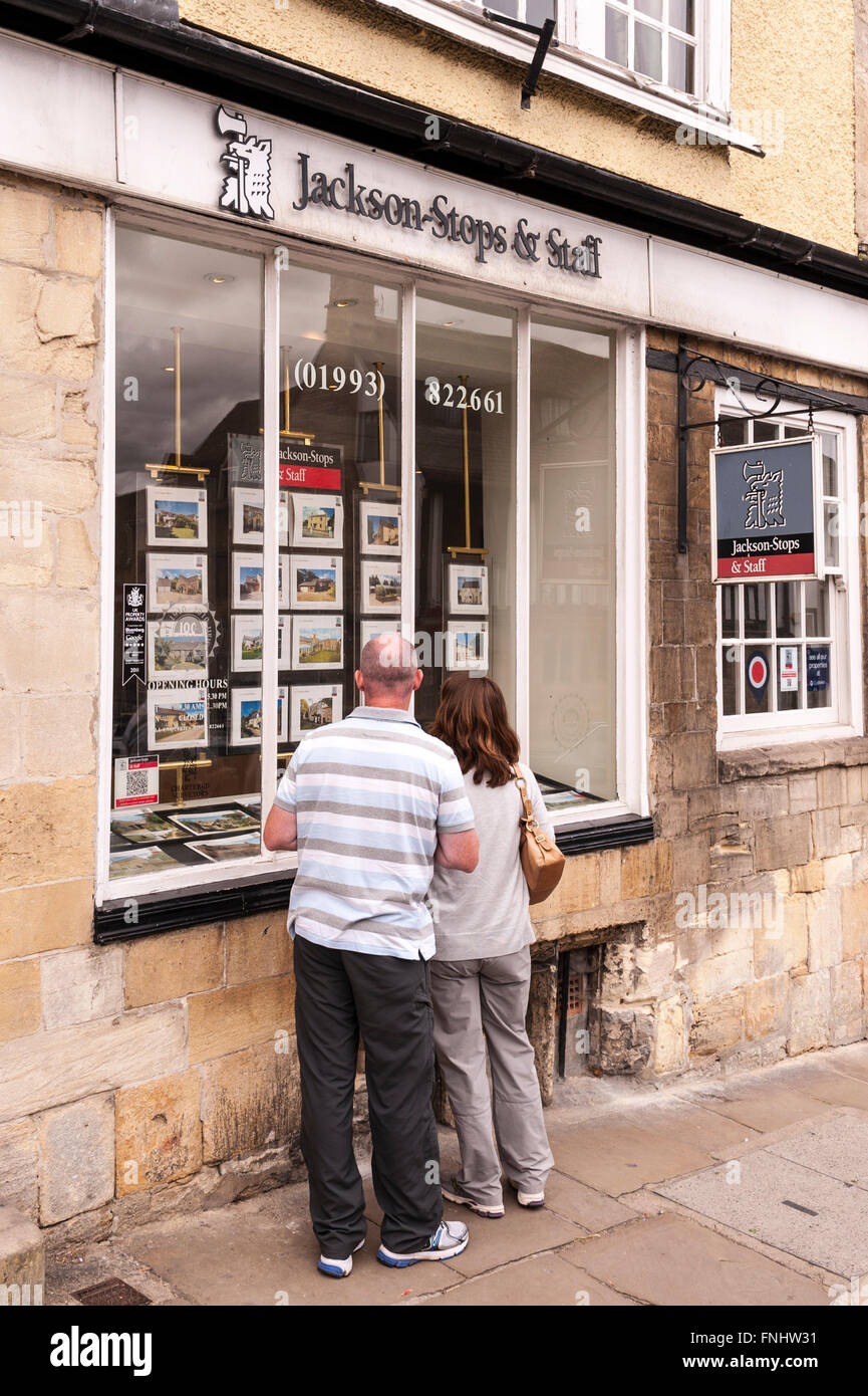 Una coppia in cerca di un agente immobiliare finestra a Burford , Oxfordshire , Inghilterra , Inghilterra , Regno Unito Foto Stock