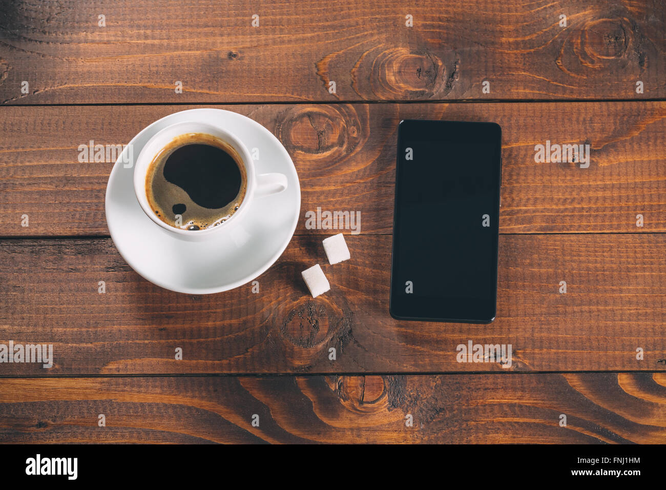 Bellissimo e nuovo nero cellulare, una tazza di caffè con due zollette di zucchero i cubi su vecchio sfondo di legno Foto Stock