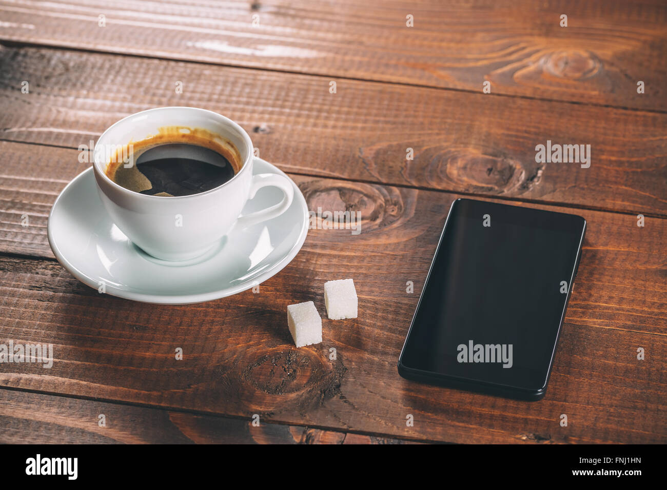 Bellissimo e nuovo nero cellulare, una tazza di caffè con due zollette di zucchero i cubi su vecchio sfondo di legno Foto Stock