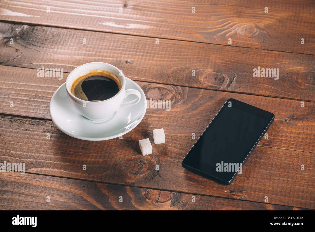 Bellissimo e nuovo nero cellulare, una tazza di caffè con due zollette di zucchero i cubi su vecchio sfondo di legno Foto Stock